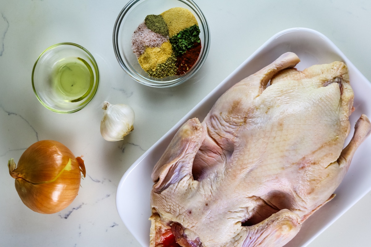 onion, garlic on the table, oil and seasoning on a glass bowl, and a duck on a white plate.