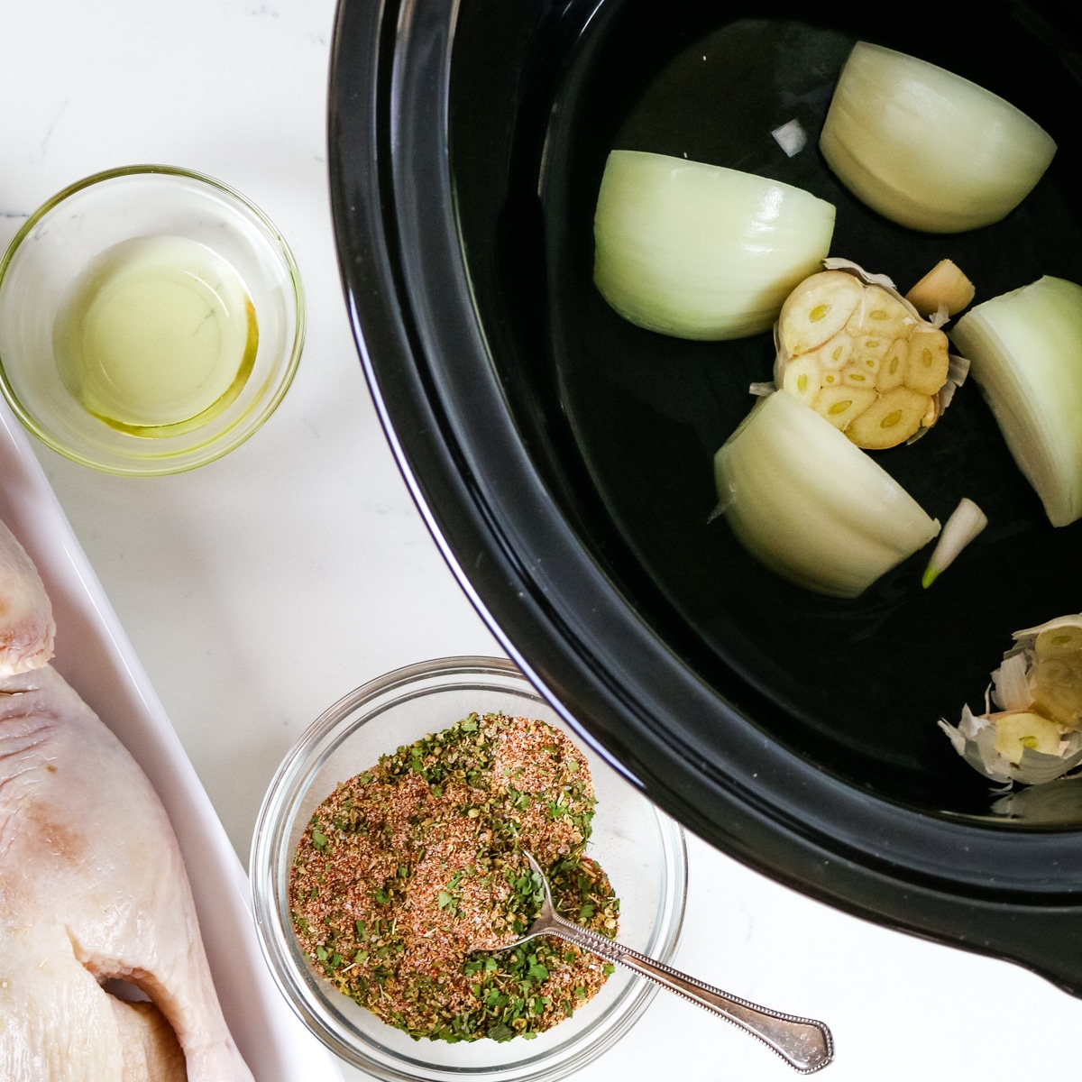 Duck on a white plate, oil & salt in a glass bowl, and garlic and onion in the slow cooker.
