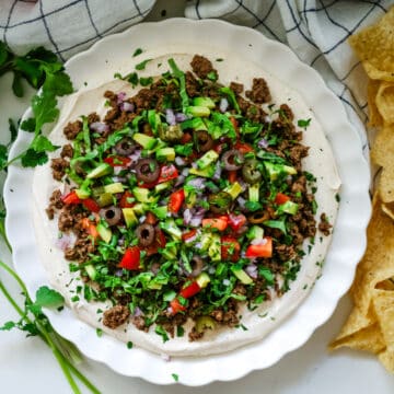 Ground beef taco dip on a white plate with nachos on the side.