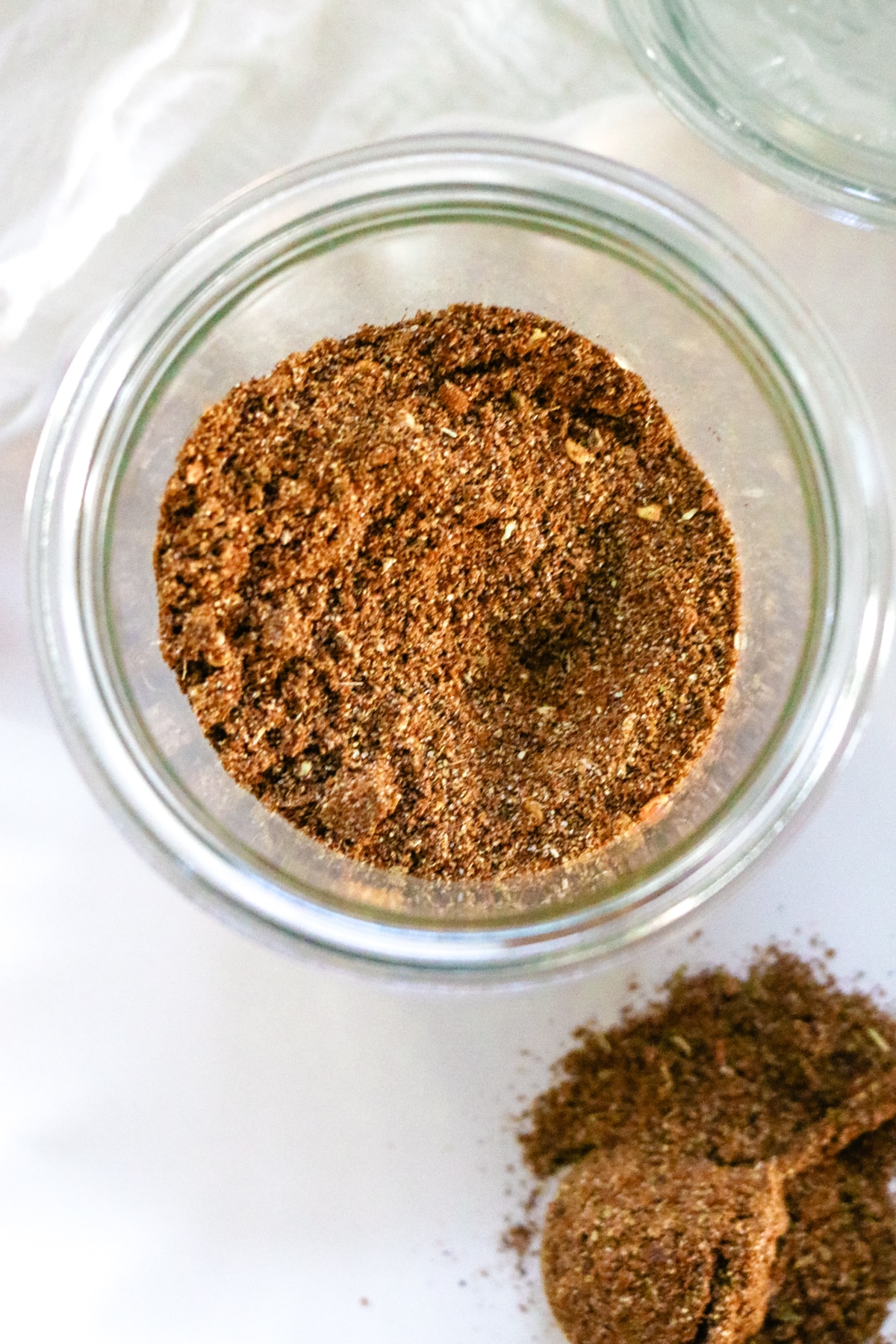 Taco seasoning in a clear glass and on a spoon on a white plate.