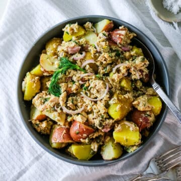 A gray bowl filled with tuna potato salad, with a spoon inside.
