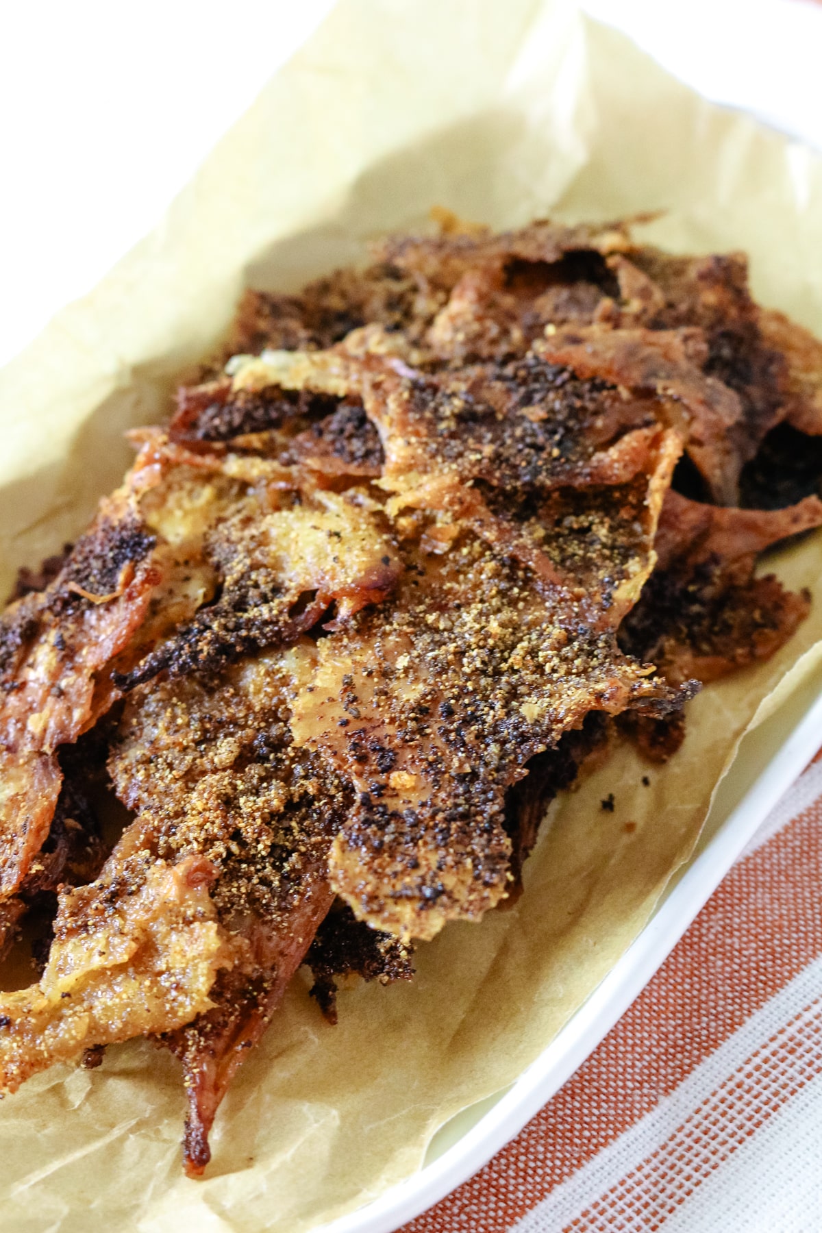 Chicken skin chips on parchment paper on a white plate.