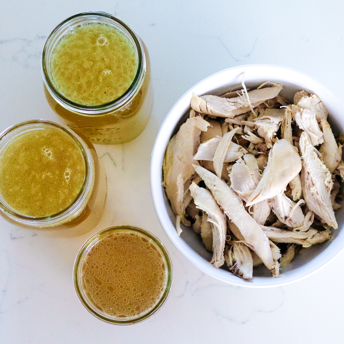 op view of two clear bowls and one clear bowl with chicken broth in it, with a chicken in a white bowl on the side.