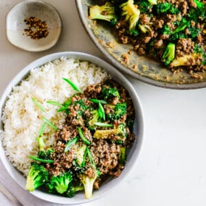 Ground beef with broccoli and rice on a plate, with extra ground beef, broccoli in a pan, and spices on the side.