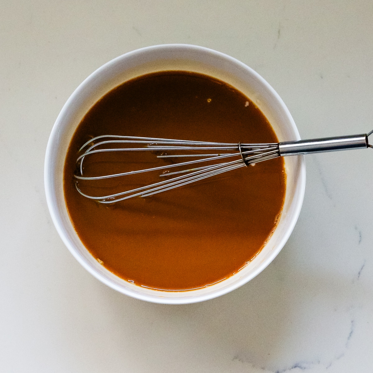 A sauce in a white bowl with a whisk inside.