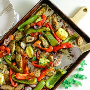 Sausage and peppers on a baking sheet, with two white plates and utensils on the side.