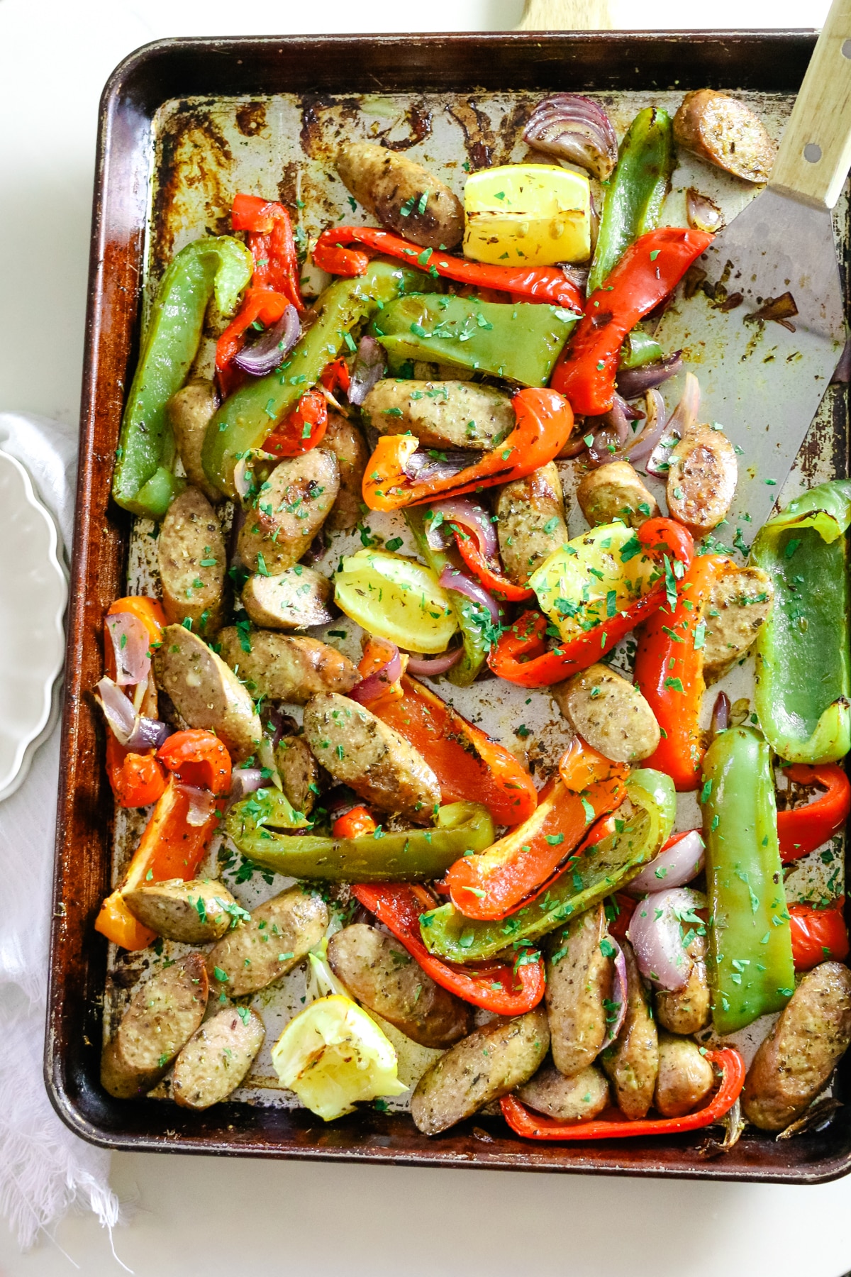 Sausage and peppers on a baking sheet, with two white plates on the side.