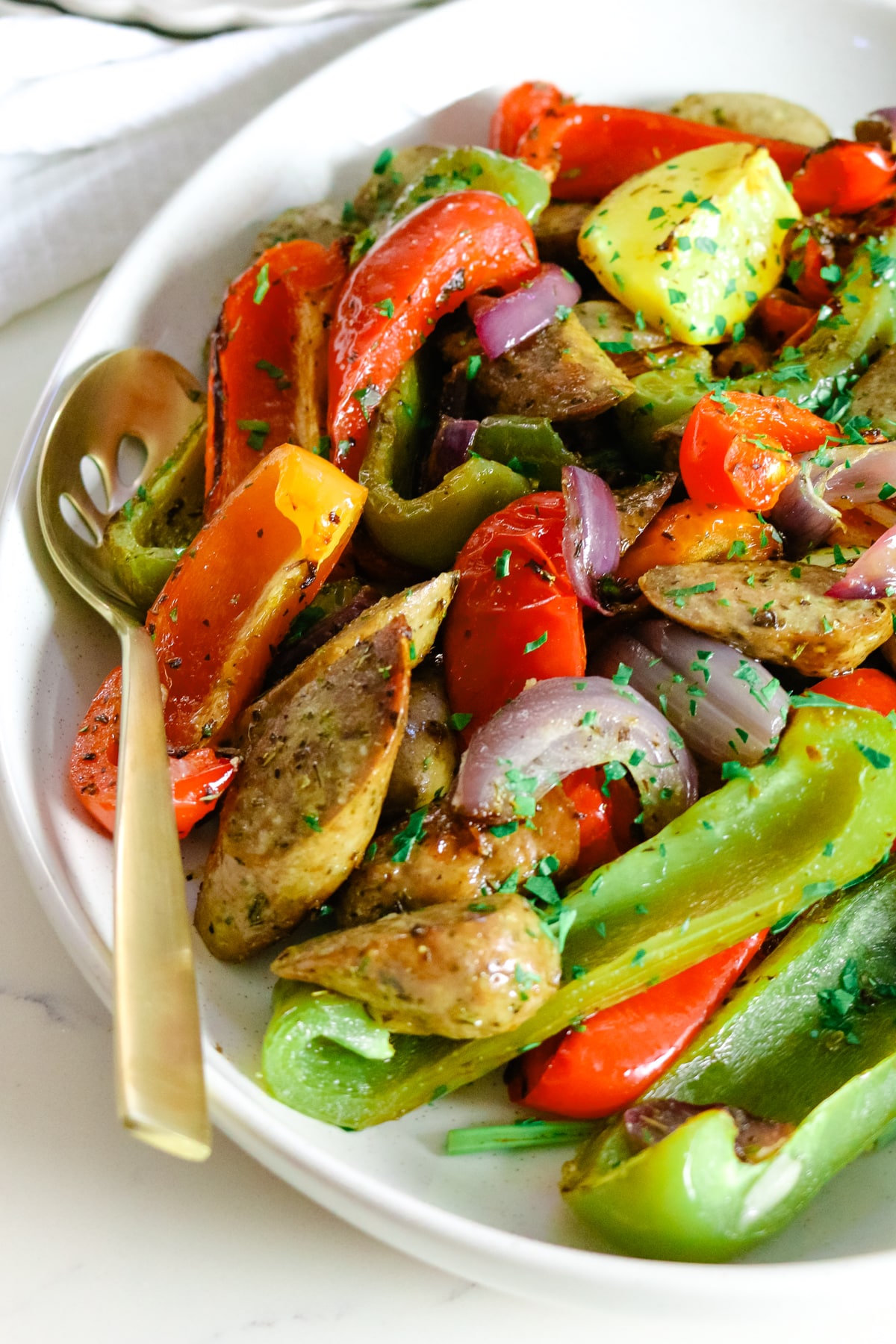 Sausage and peppers on a white plate, with a spoon in it.