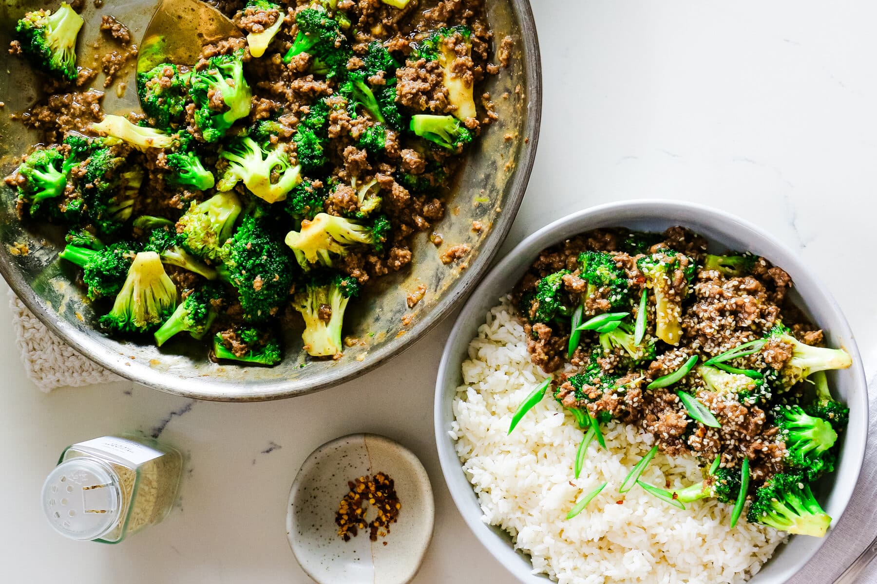 Ground beef with broccoli and rice on a plate, with extra ground beef, broccoli in a pan, and spices on the side.