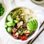 Ahi tuna poke in a white bowl, with mayonnaise, chopsticks on the side, and green onion leeks in a beige bowl.