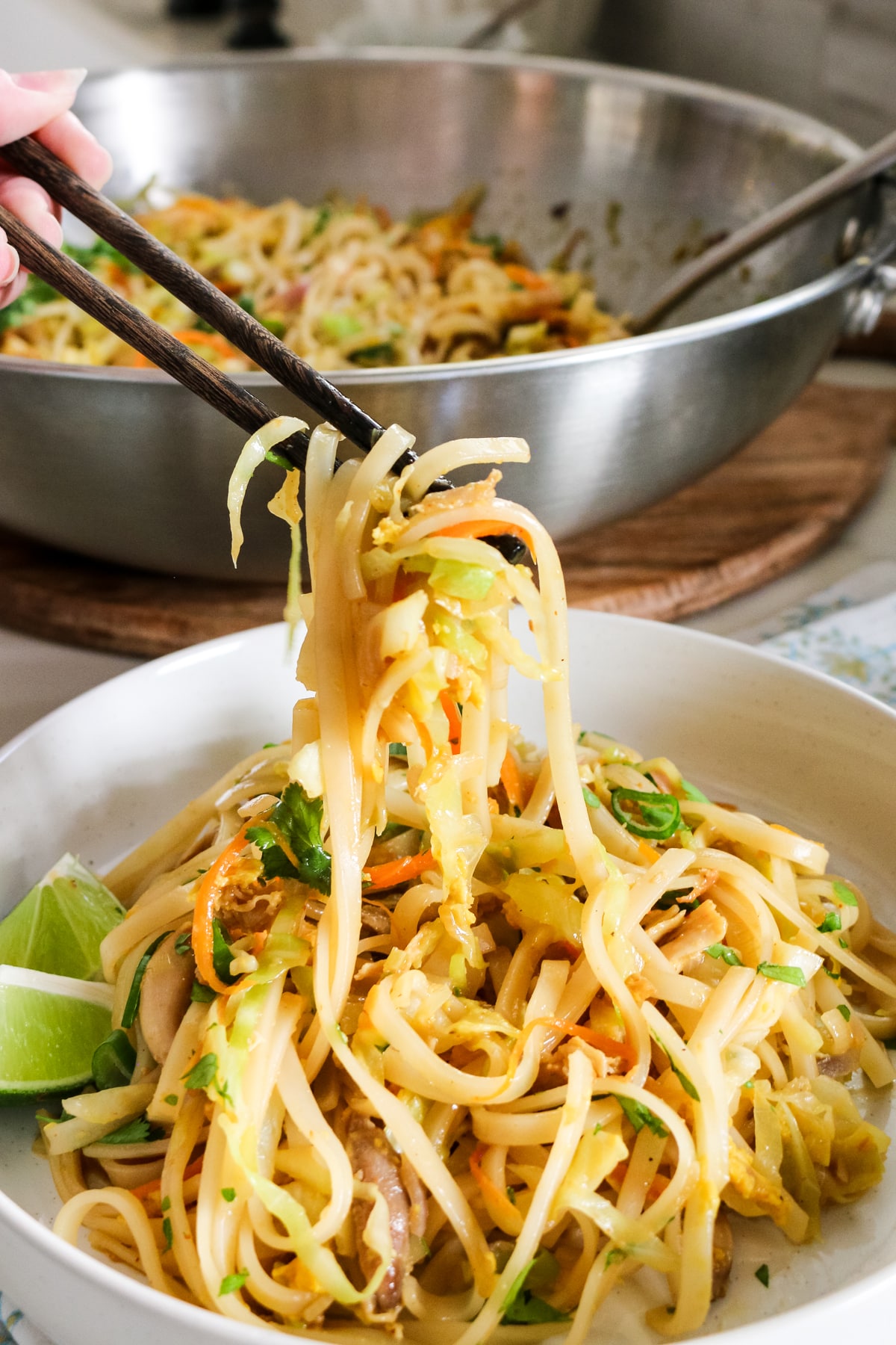 Chicken Pad Thai in a white bowl with chopsticks lifting some noodles.