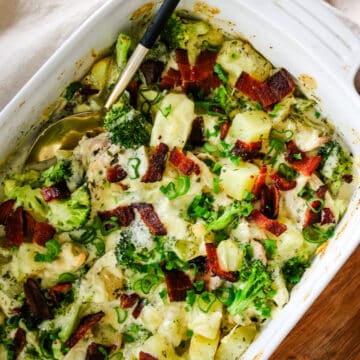 Baked chicken, potatoes, and broccoli in a baking pan with a serving spoon in it.