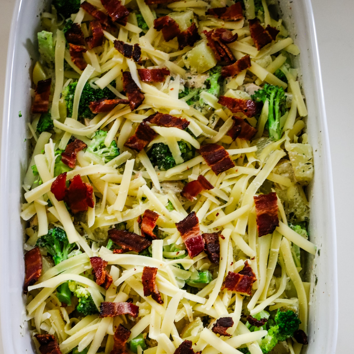 Boiled potatoes, broccoli, and chicken in a baking pan, topped with grated cheese.
