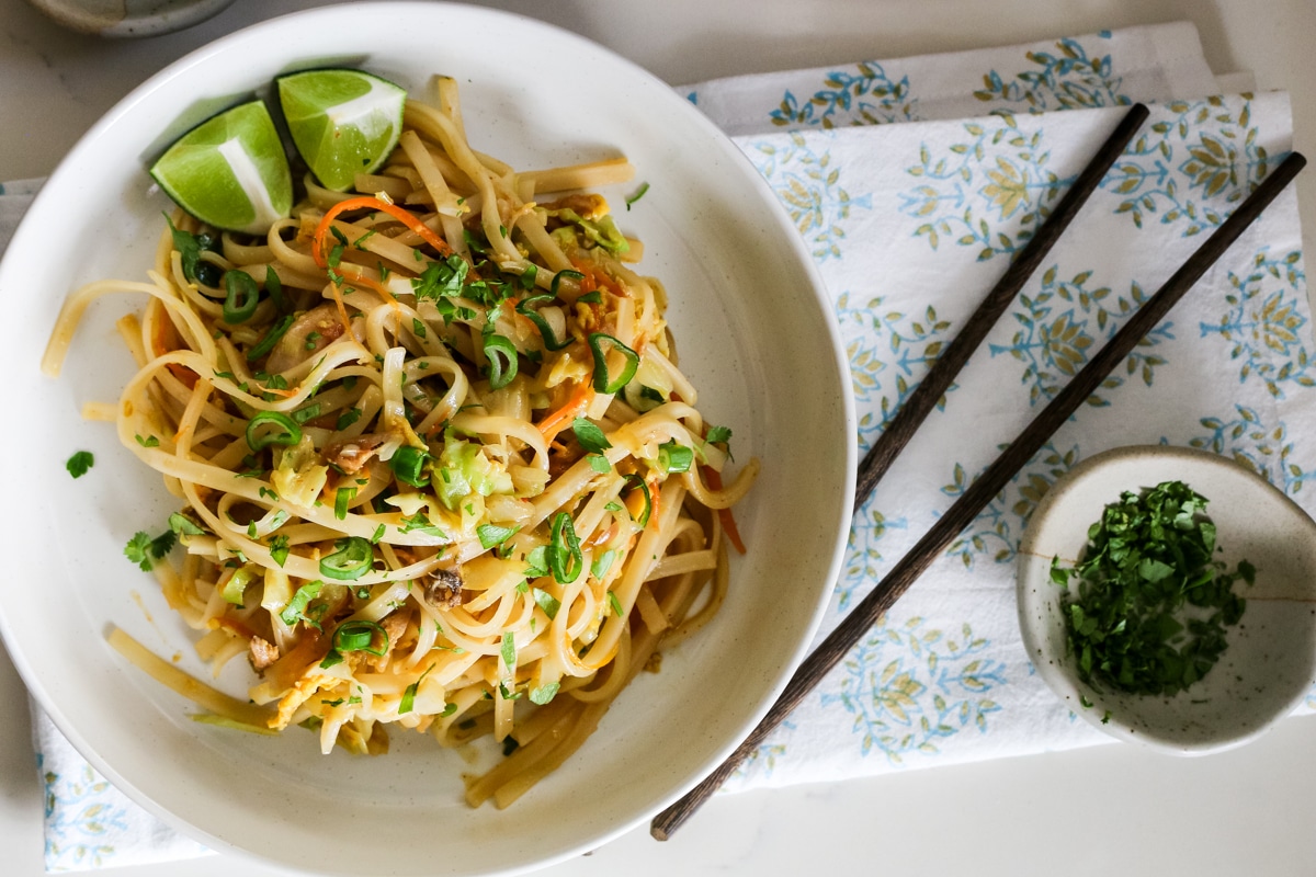 Chicken Pad Thai in a white bowl with chopsticks beside it.