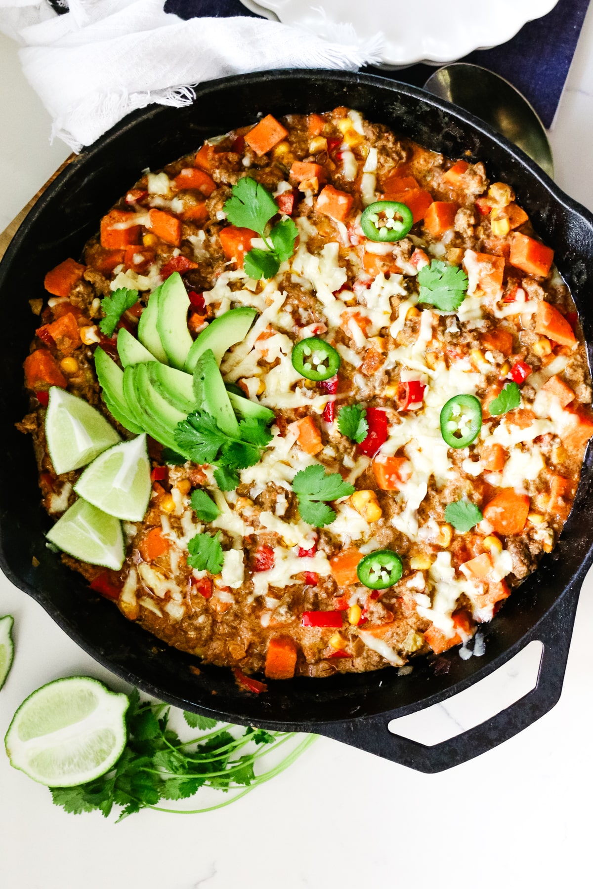 Ground beef and sweet potato in a skillet with lime and parsley beside it.