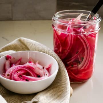 Pickled red onions in a white bowl and in a clear jar beside it.