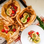Fish en papillote in parchment paper, served on a white plate with a fork.