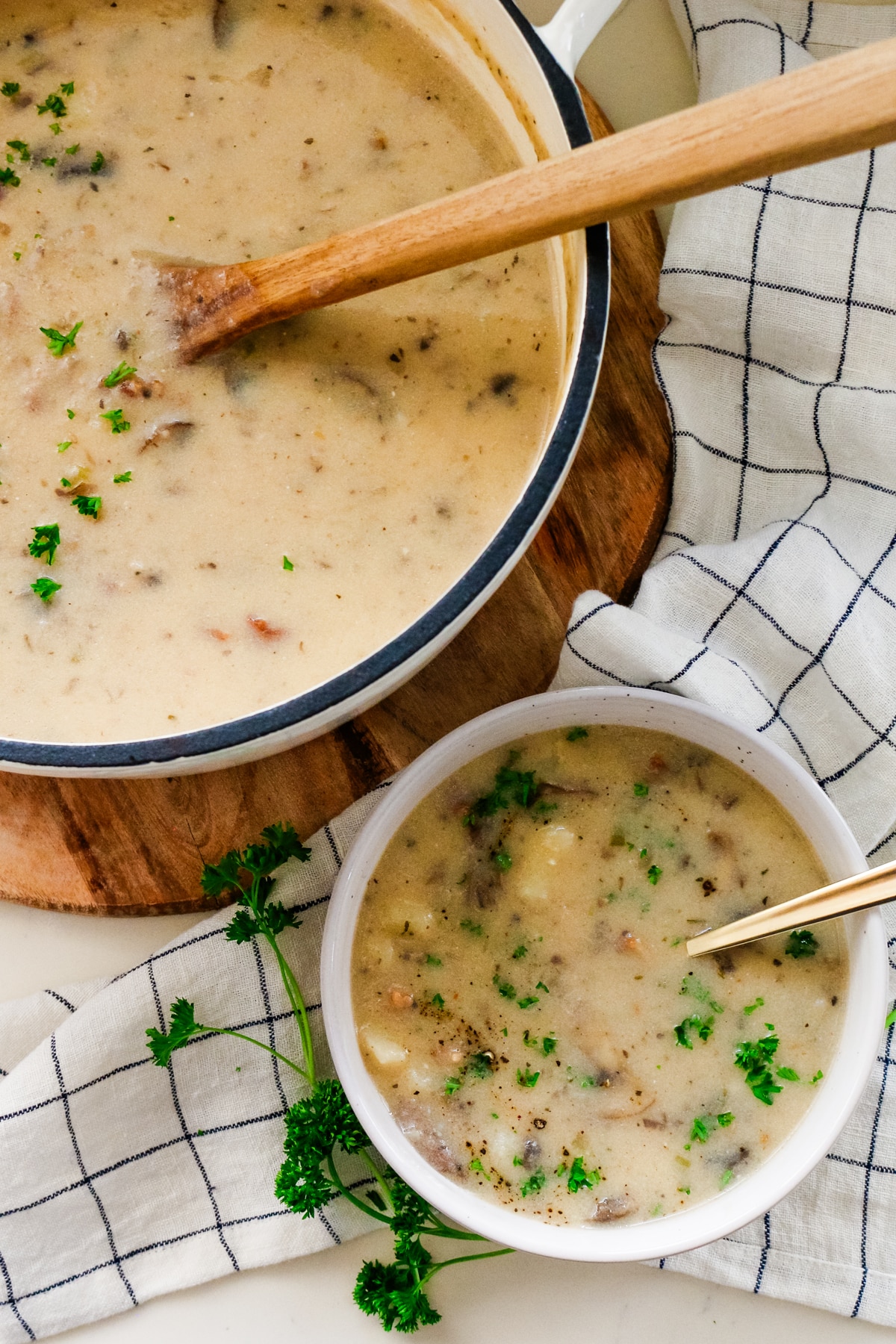 A pot of creamy mushroom, potato, and bacon soup, and a bowl of soup with a spoon in it.