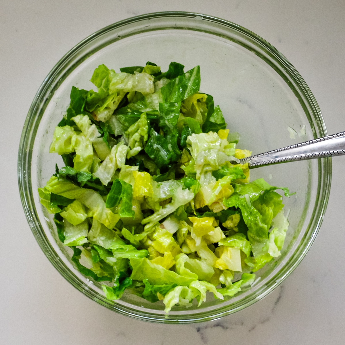 Mixing romaine lettuce in a clear bowl.