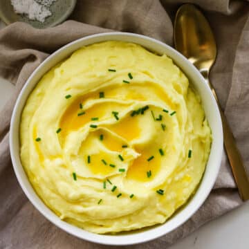 Mashed potatoes in a white bowl with a spoon beside it.