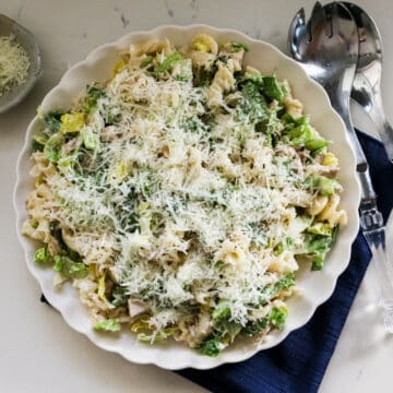 Chicken Caesar pasta salad on a white plate, topped with cheese and served with a fork beside it.
