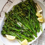 Roasted broccoli with lemon and a fork on a white platter.