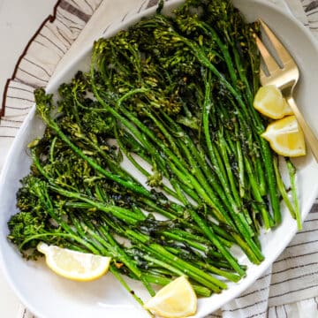 Roasted broccoli with lemon and a fork on a white platter.