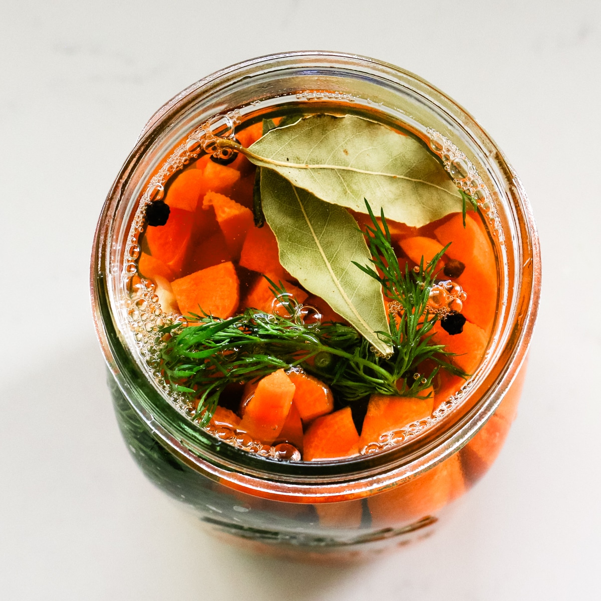 Slices of carrots inside a clear jar with laurel leaves and pepper.