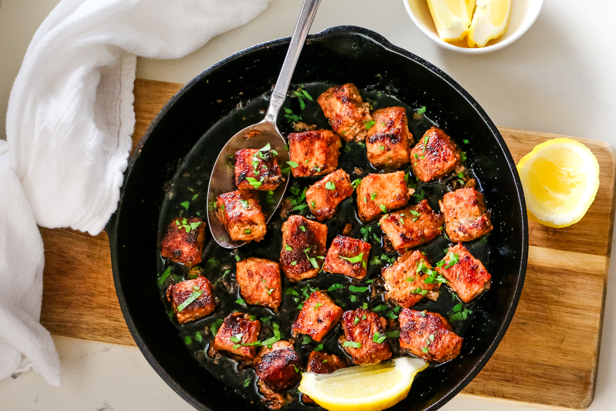 pork bites in cast iron skillet with spoon.