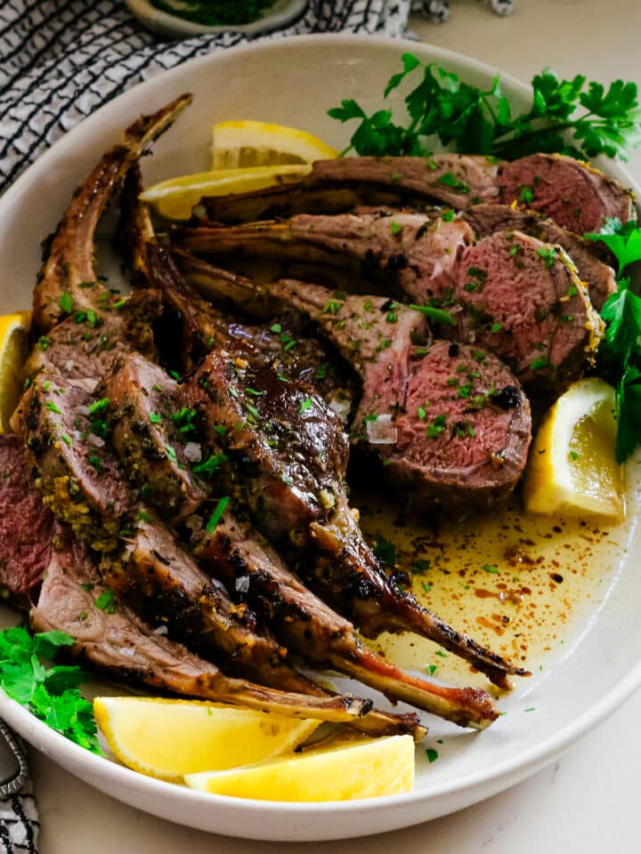 roasted rack of lamb on a plate with lemon and cilantro on the side.