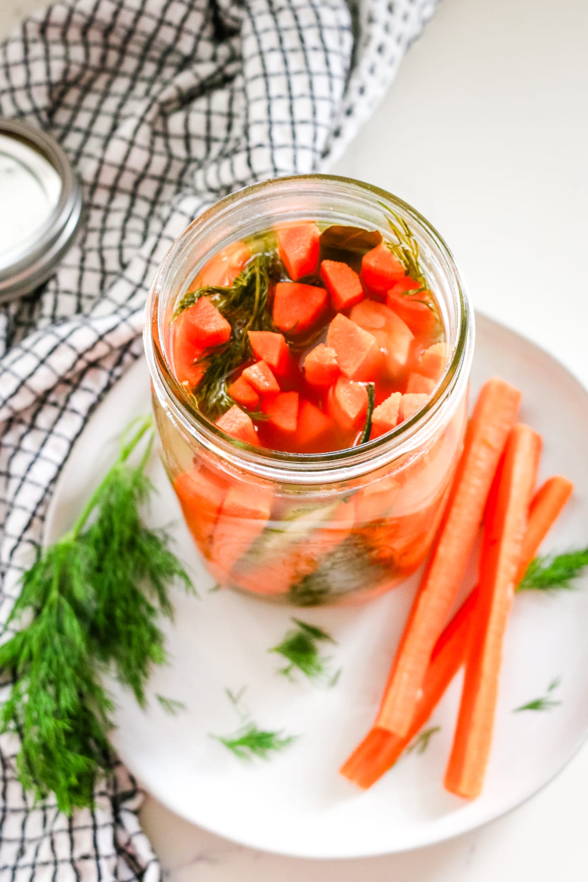 Slices of carrots on the side of an airtight jar of carrots, placed on a white plate.