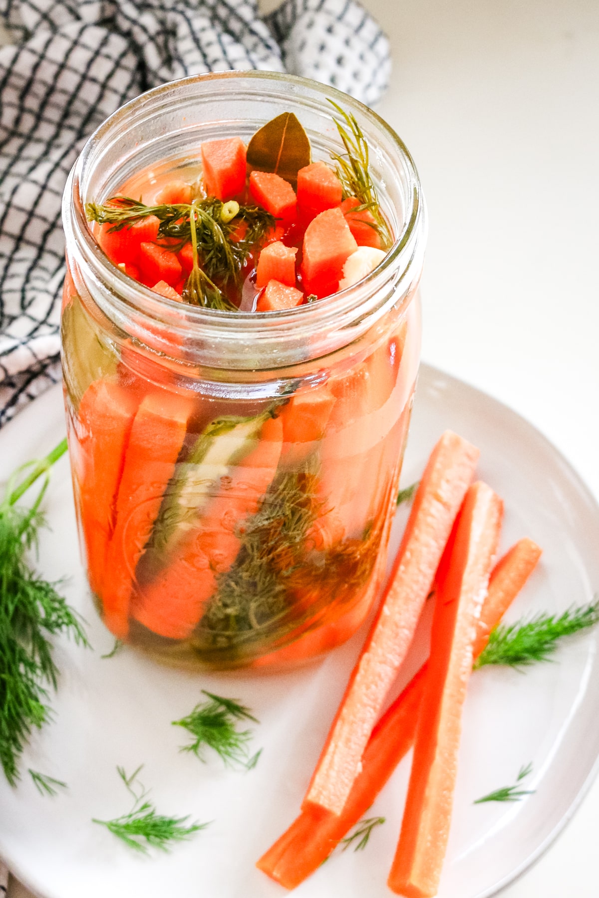 Slices of carrots on the side of an airtight jar of carrots, placed on a white plate.