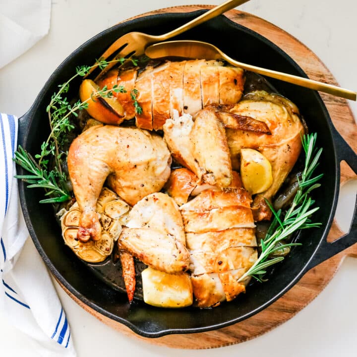 oven roasted chicken in a cast iron skillet with serving utensils.