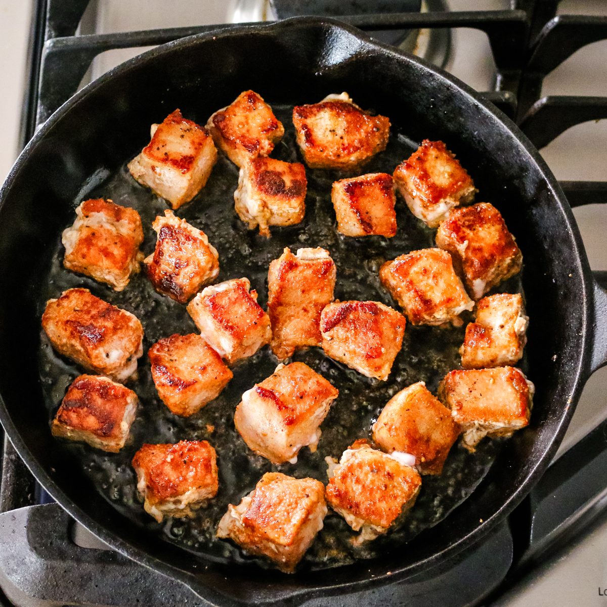 pork bites cooking in oil in a cast iron skillet.