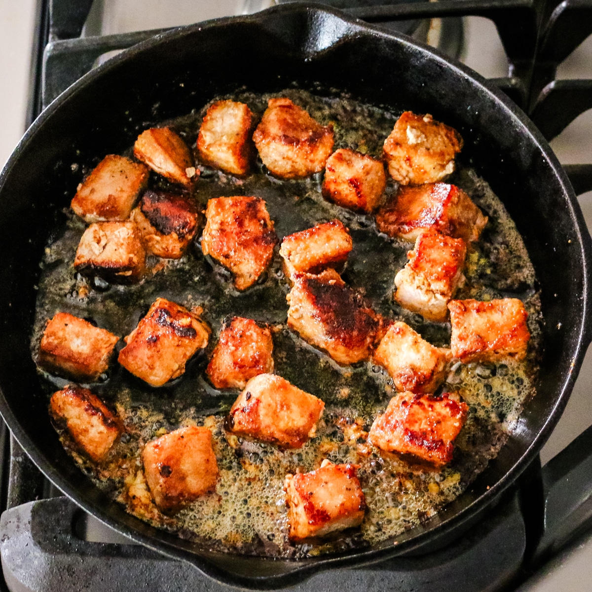 pork bites cooking in cast iron skillet.