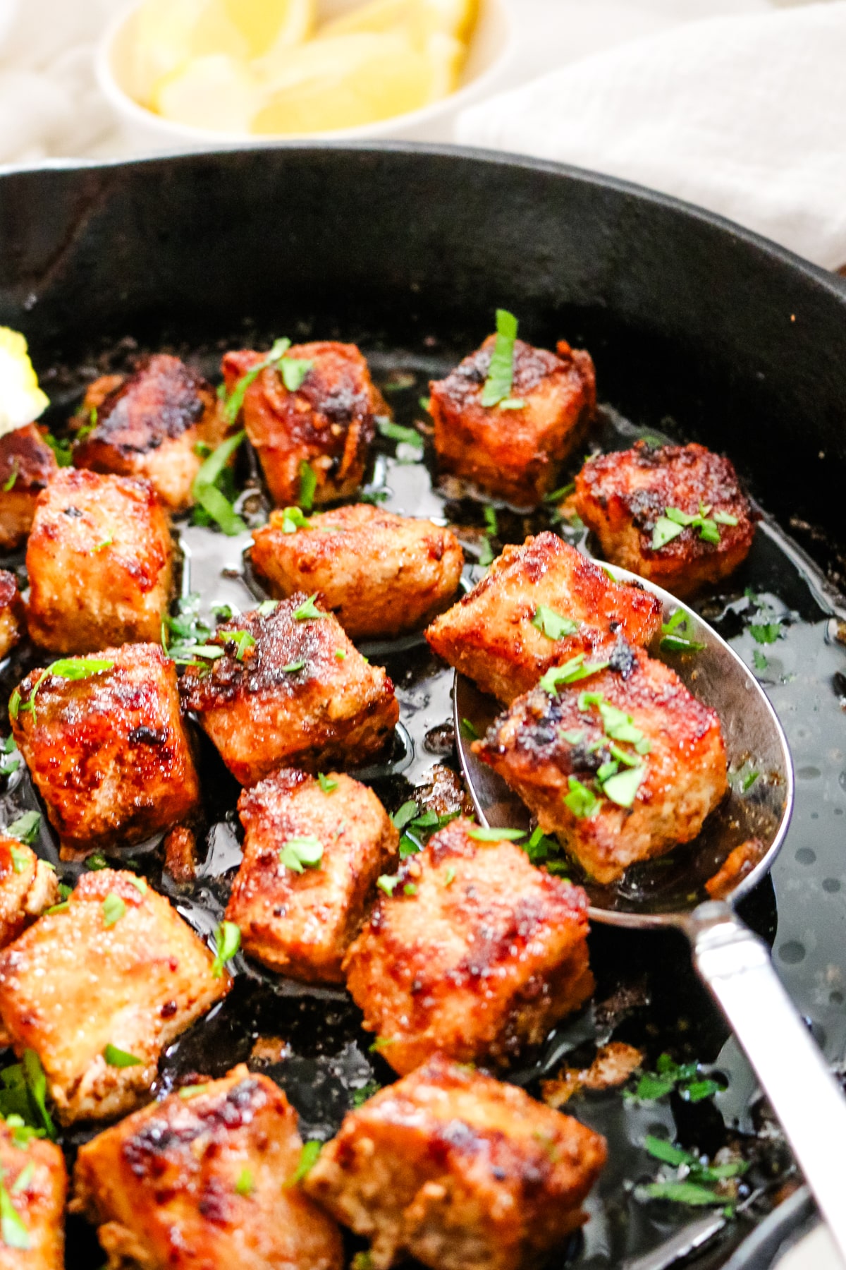 pork bites in cast iron skillet with a metal spoon.