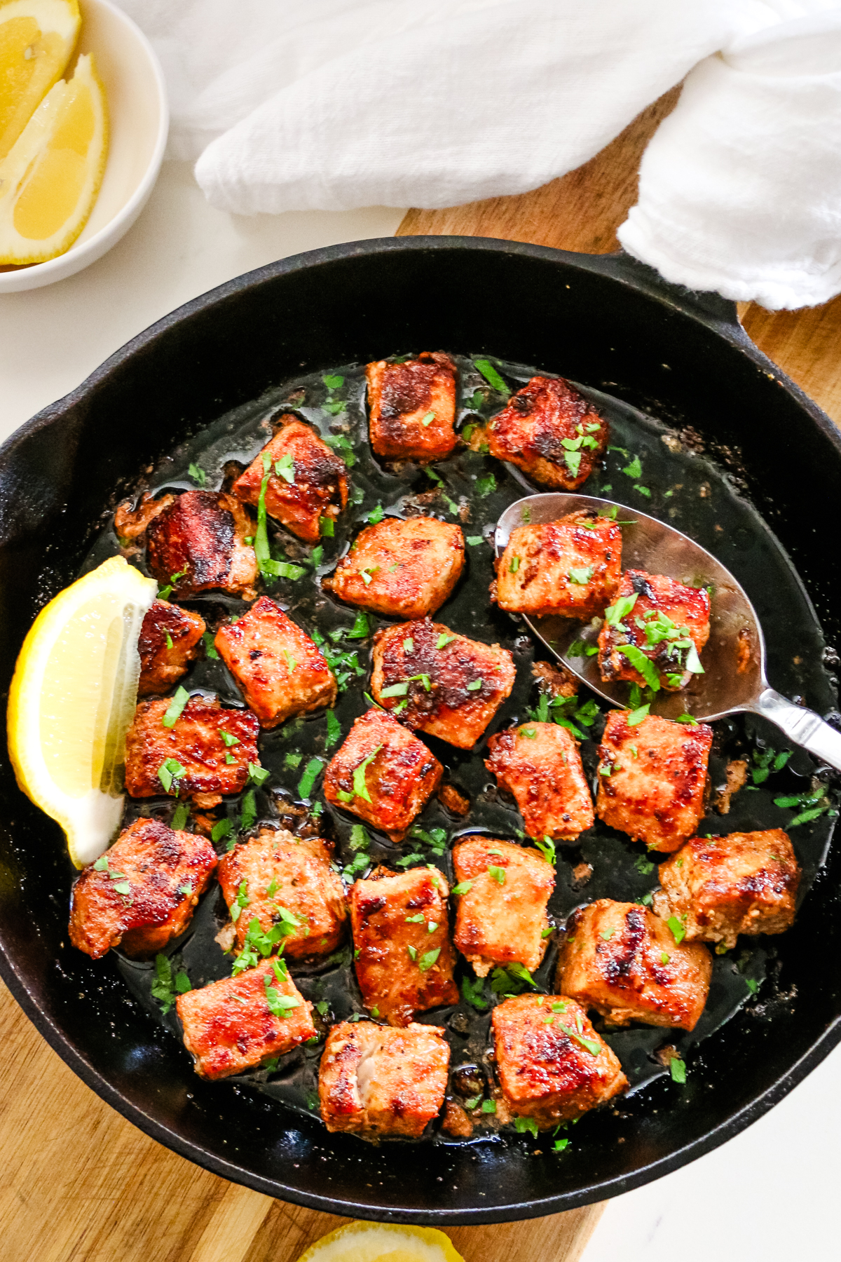 pork bites in cast iron skillet with metal spoon.