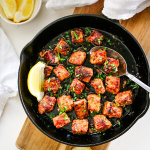 pork bites in cast iron skillet with metal spoon.