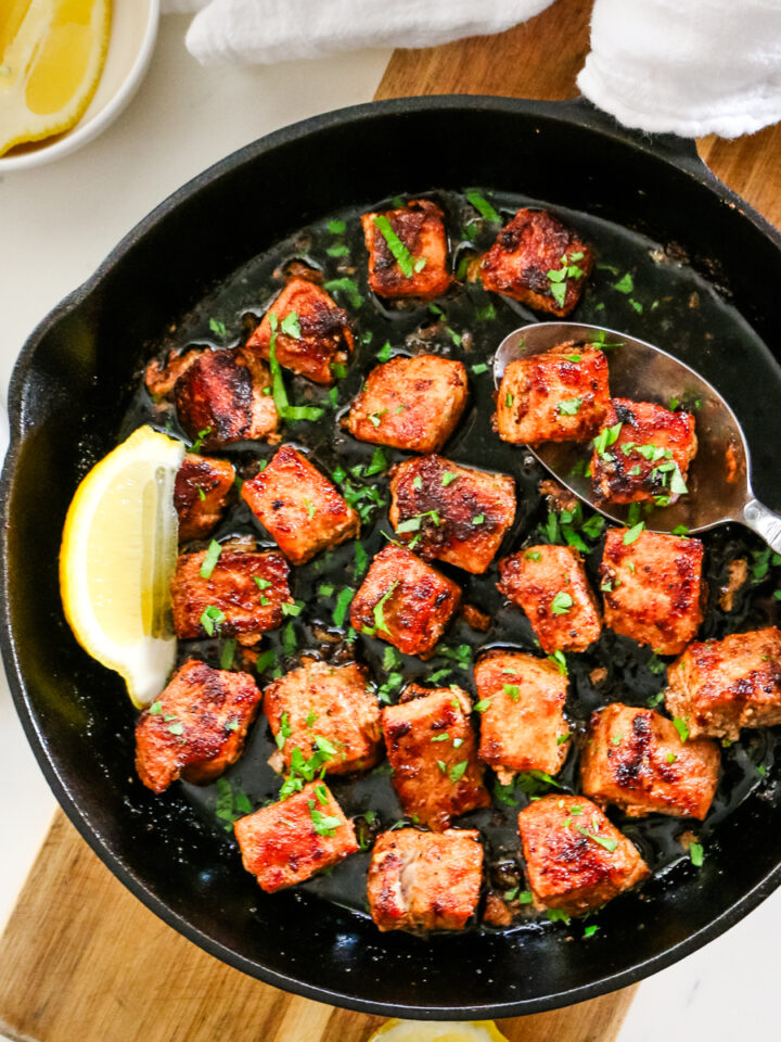 pork bites in cast iron skillet with metal spoon.
