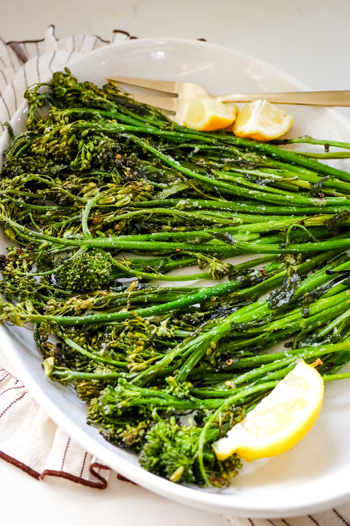 Roasted broccoli with lemon and a fork on a white platter.