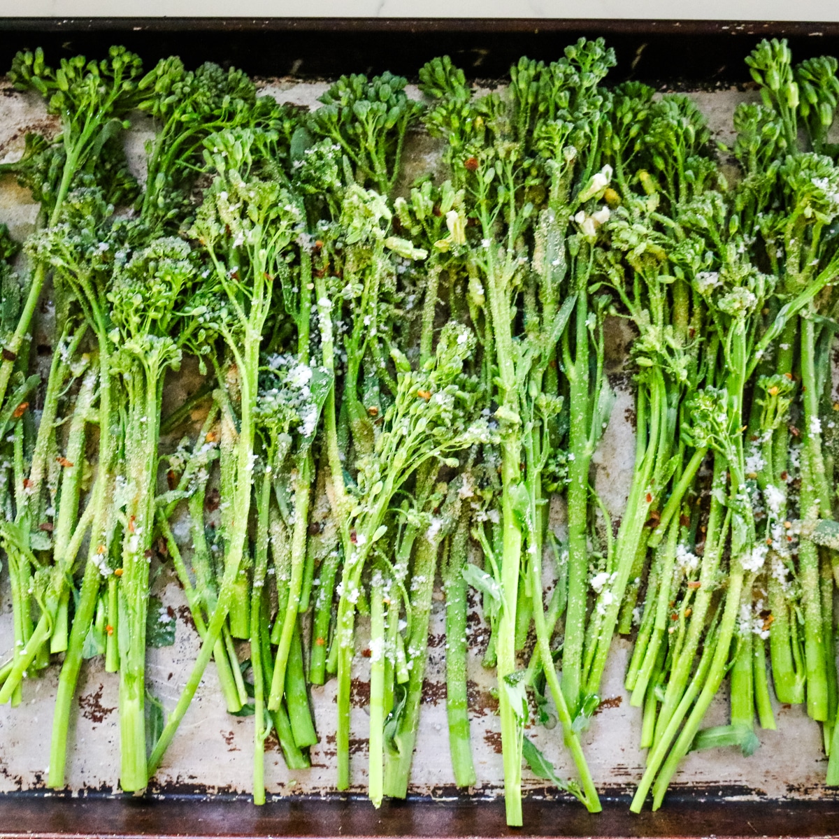 Seasoned broccolini on a baking sheet.