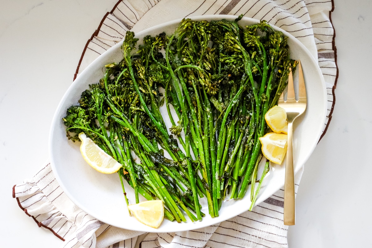 Roasted broccoli with lemon and a fork on a white platter.