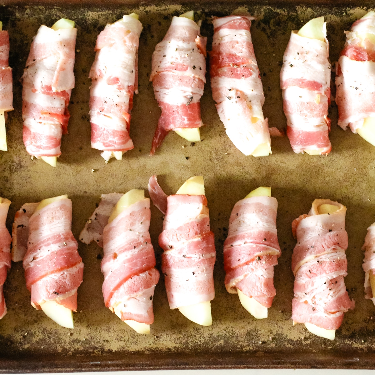 uncooked bacon wrapped potatoes on a baking pan.