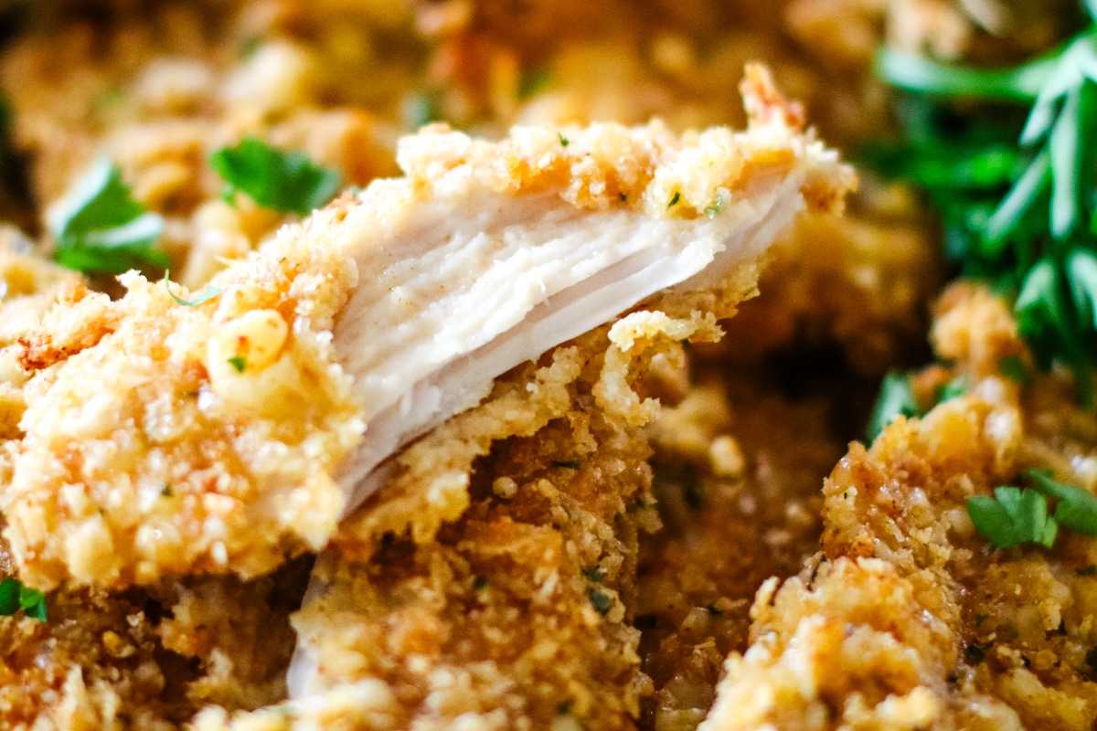 crispy oven-baked chicken cutlets on a plate with one cutlet broken in half .