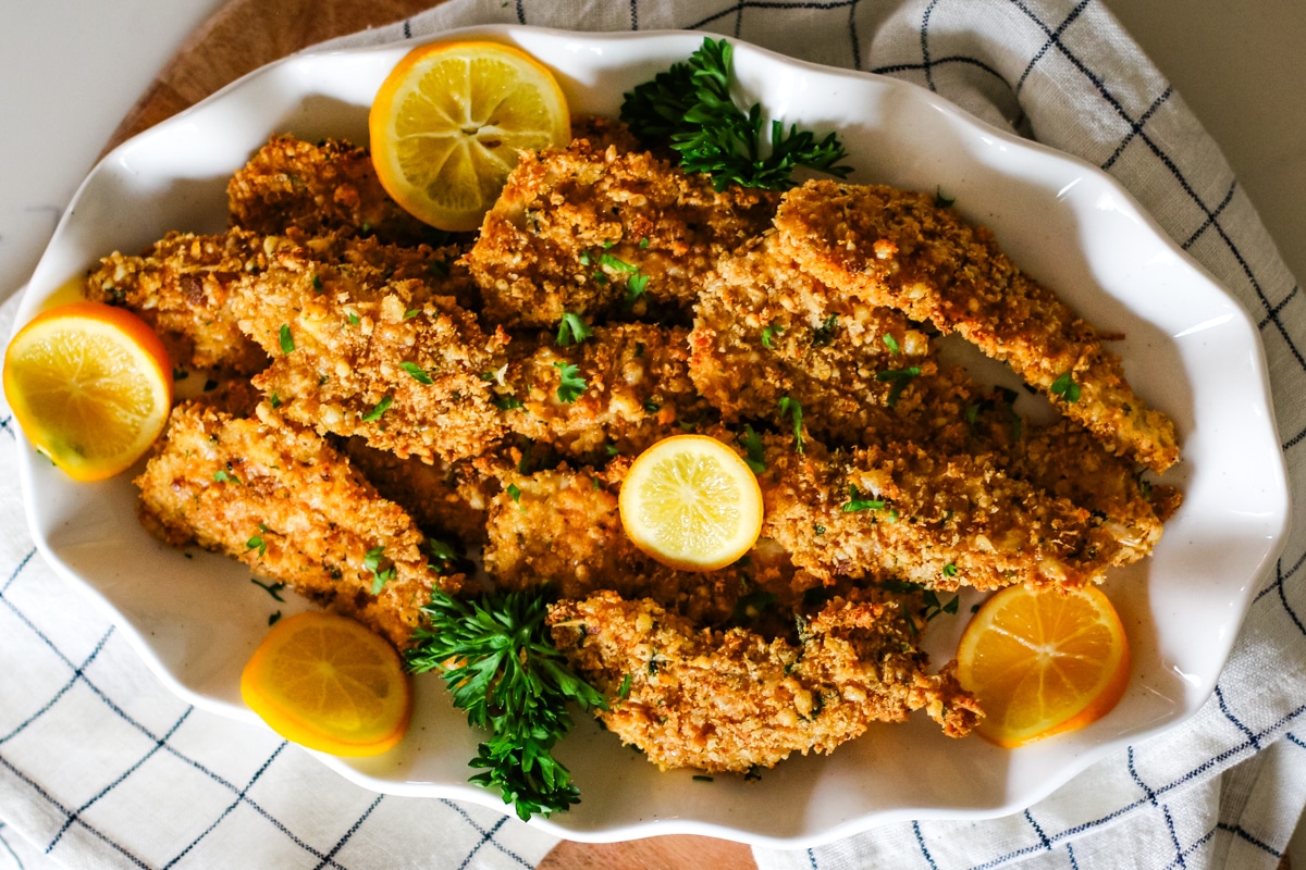 crispy oven-baked chicken cutlets on a plate with lemon slices and fresh parsley.