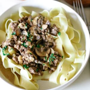 pasta with ground beef stroganoff in a small bowl topped with herbs.