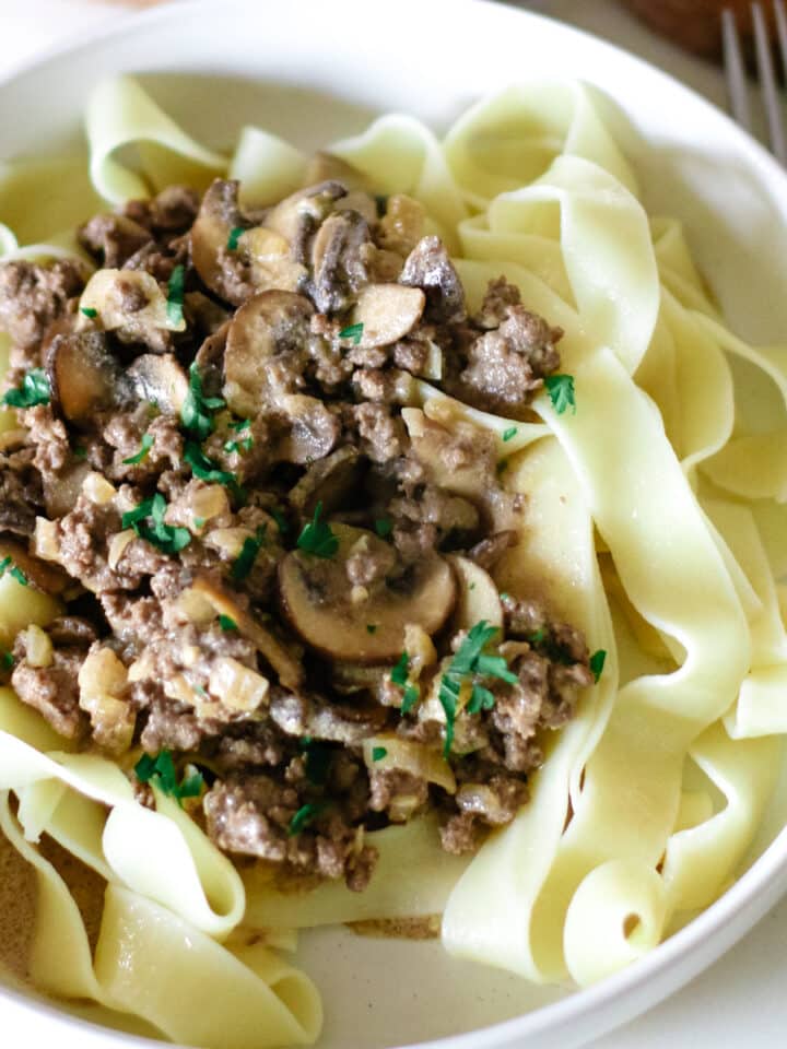pasta with ground beef stroganoff in a small bowl topped with herbs.