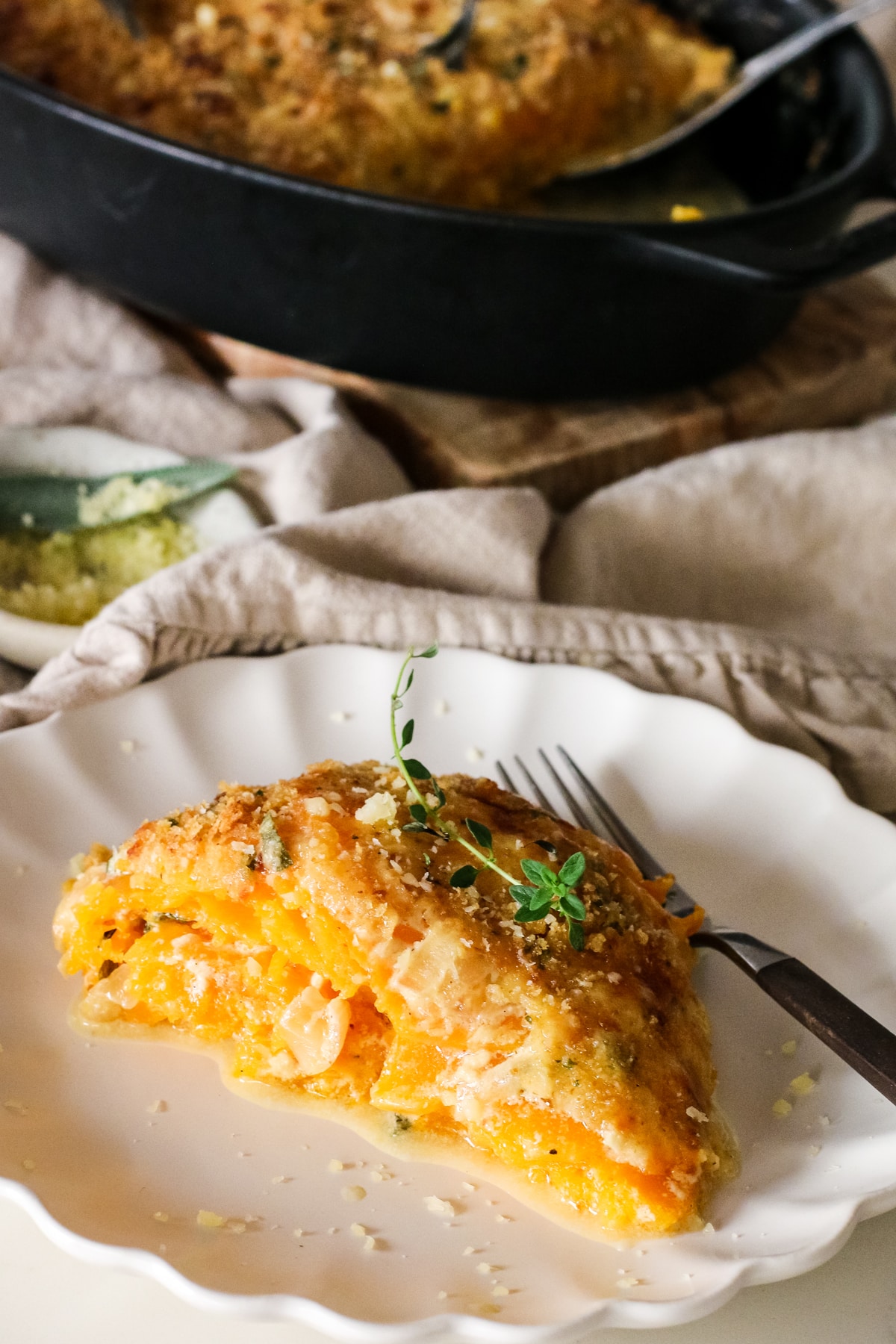 butternut squash gratin slice on a plate with a fork infront of baking dish.