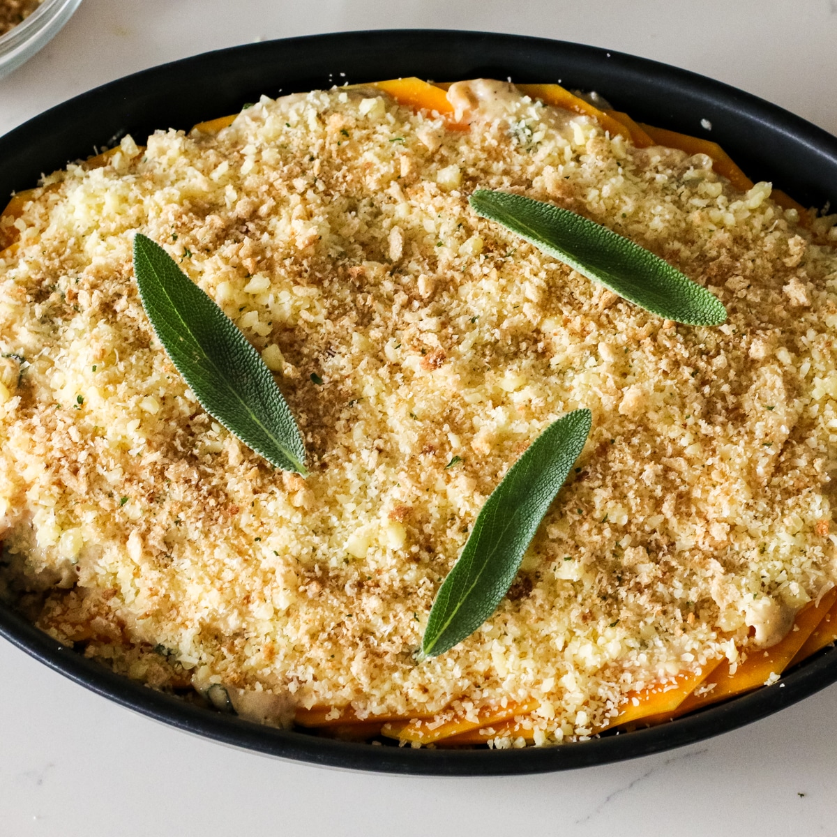 carmalized onion sauce covering the squash slices with bread crumbs on top, in a baking dish.