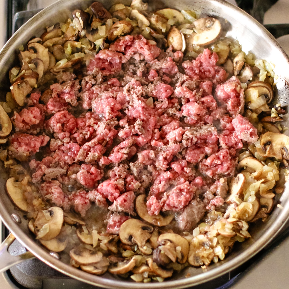 cooking beef and mushrooms in a stainless steel pan.